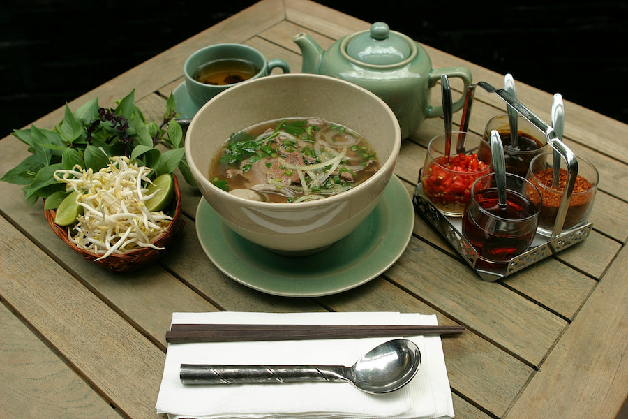 Bowl of pho noodle soup with condiments around it