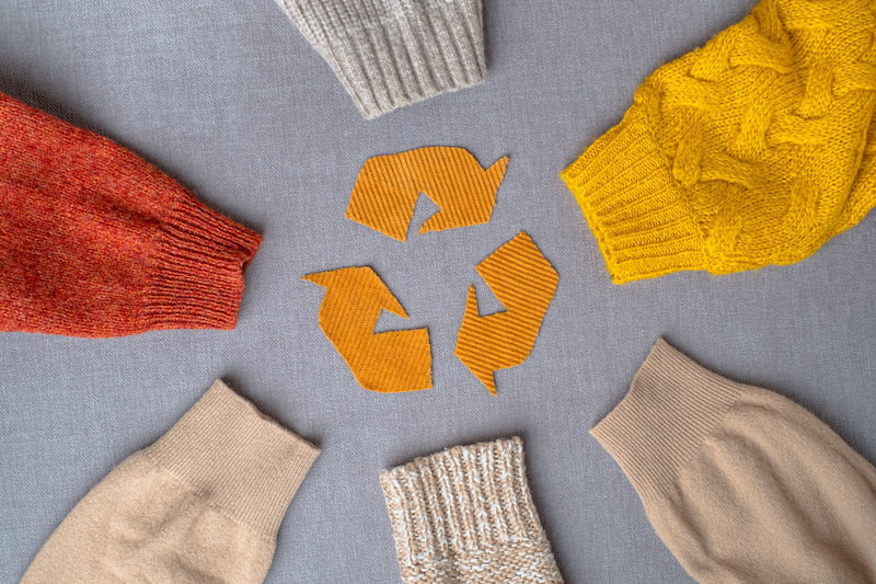 Recycling symbol in fabric surrounded by sleeves of sweaters