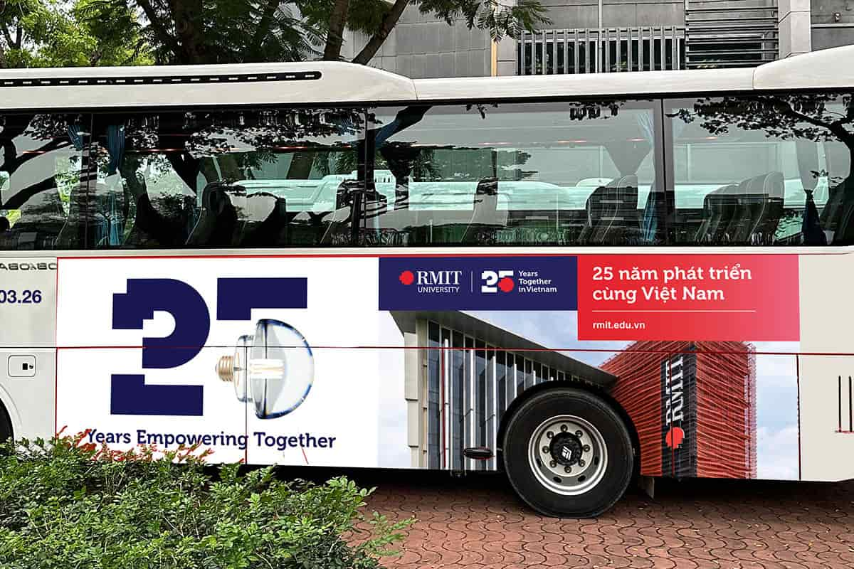 The RMIT shuttles at the Saigon South campus, with 25th anniversary branded decals on it, showcasing the anniversary logos, "25 years in VIetnam" in Vietnamese, the rmit URL and an image of RMIT Building 2 in the backdrop. 