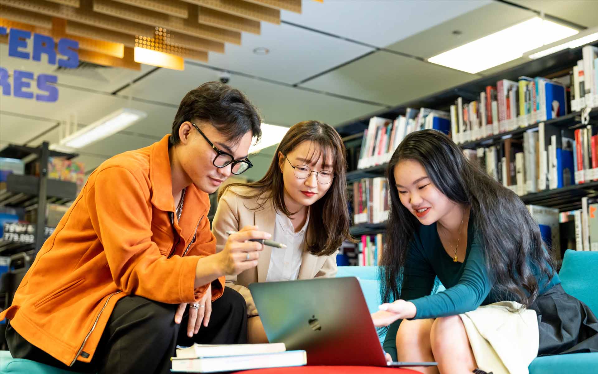 three students one male and two female having a discussion in a library