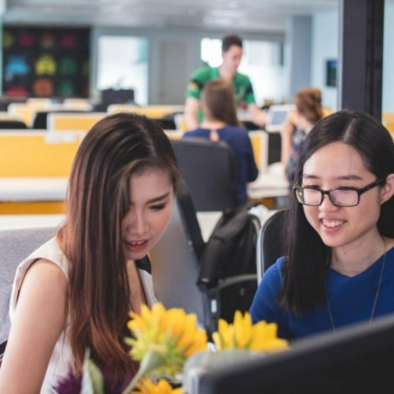 two girls working in the office with three colleagues in the background