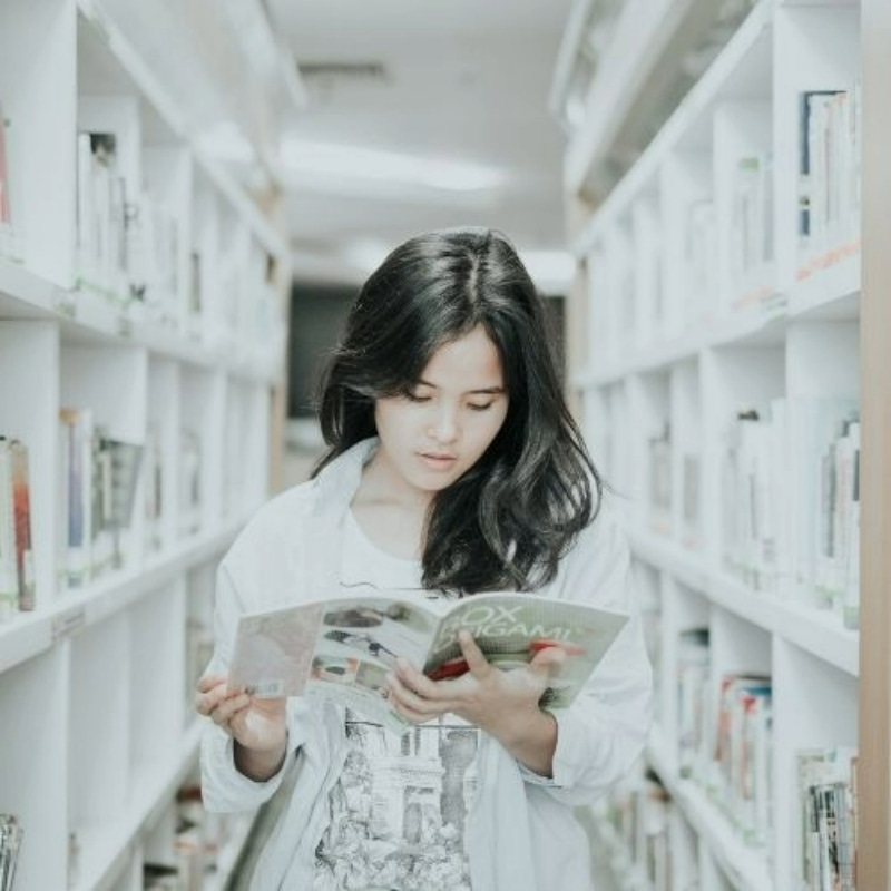 a female student reading a book titled box origami in the library